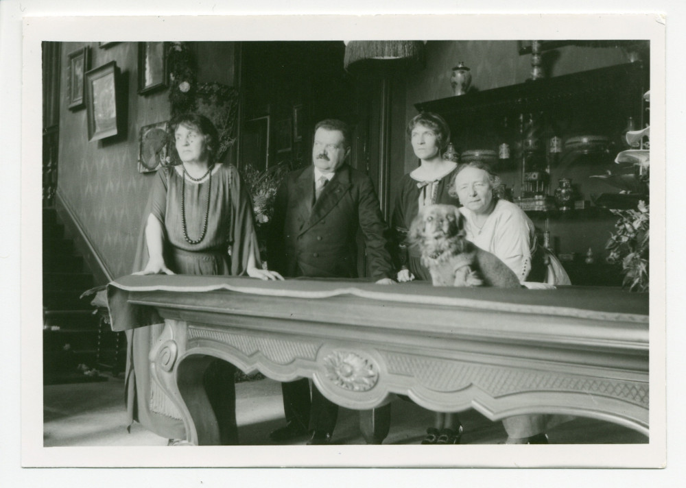 Photographie d'Hélène Gorska avec (de gauche à droite) le Dr Orowski, Mme Vaslav Gorska (sa belle-fille), Antonina Wilkonska et le chien Ping, dans le hall de Riond-Bosson, avec la table de billard et au fond l'escalier menant aux appartements privés