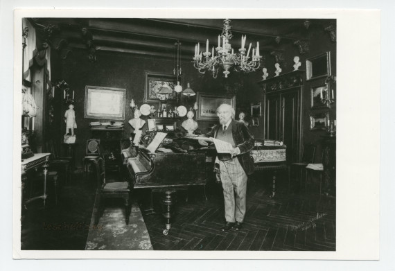 Photographie de Teodor Leszetycki (1830-1915), âgé, debout avec une partition, sans doute dans son salon de musique avec 2 pianos