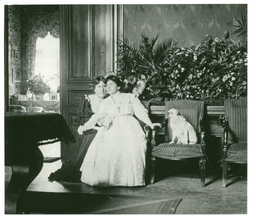 Photographie d'Hélène Paderewska assise dans le hall de Riond-Bosson avec une inconnue (Mme Obuchowicz?) et sa chienne Manon