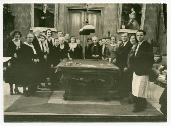 Photographie de Paderewski distribuant des cadeaux aux employés de Riond-Bosson autour de la table de billard, dans le hall, avec en arrière-fond les portraits d'Ignace et de Hélène Paderewski par Charles Giron, lors du réveillon 1930