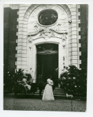 Photographie d'Hélène Paderewska tenant son chien Ping dans ses bras devant l'entrée principale de Riond-Bosson, avec à ses côtés un landau conduit par un homme non identifié
